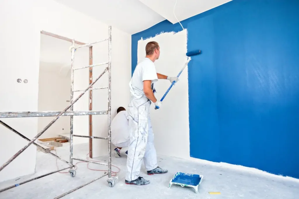 Painters applying blue paint to a wall.