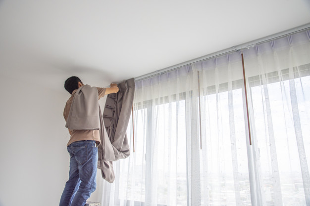 Adding the finishing touch: A person hangs a new curtain, enhancing the privacy and aesthetic of a window.