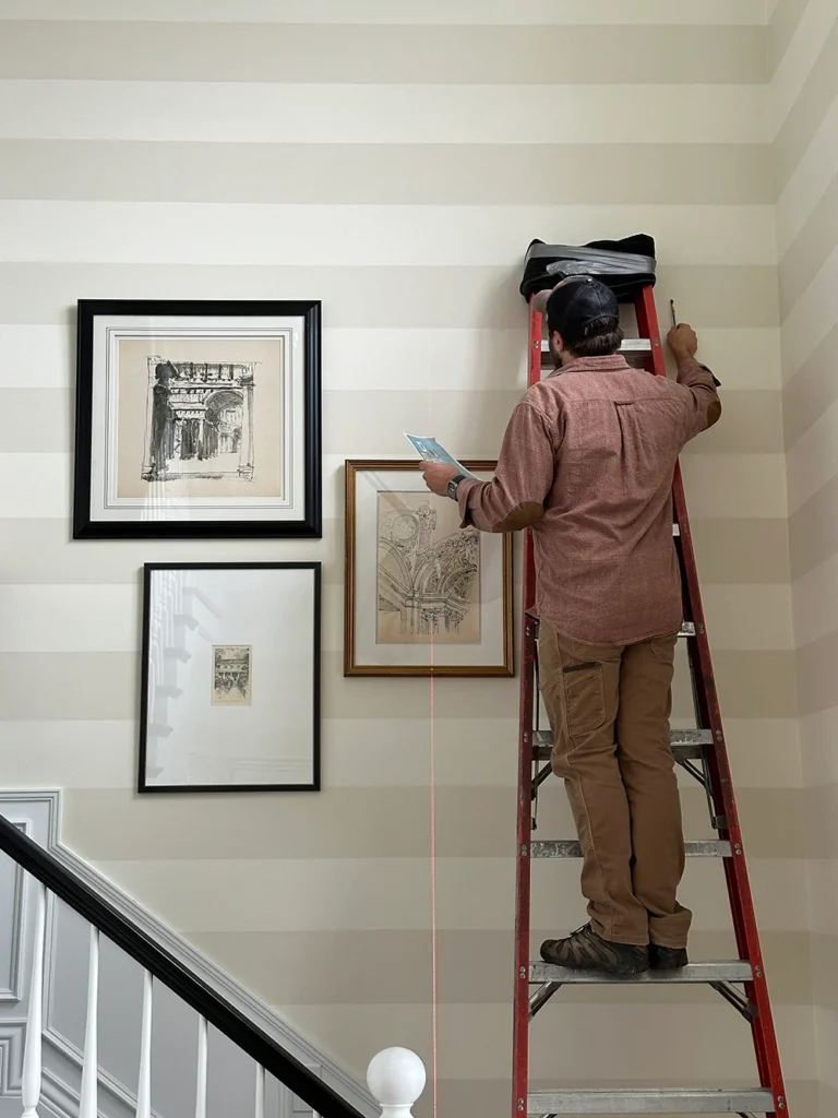 Man on ladder hanging pictures with a laser level.