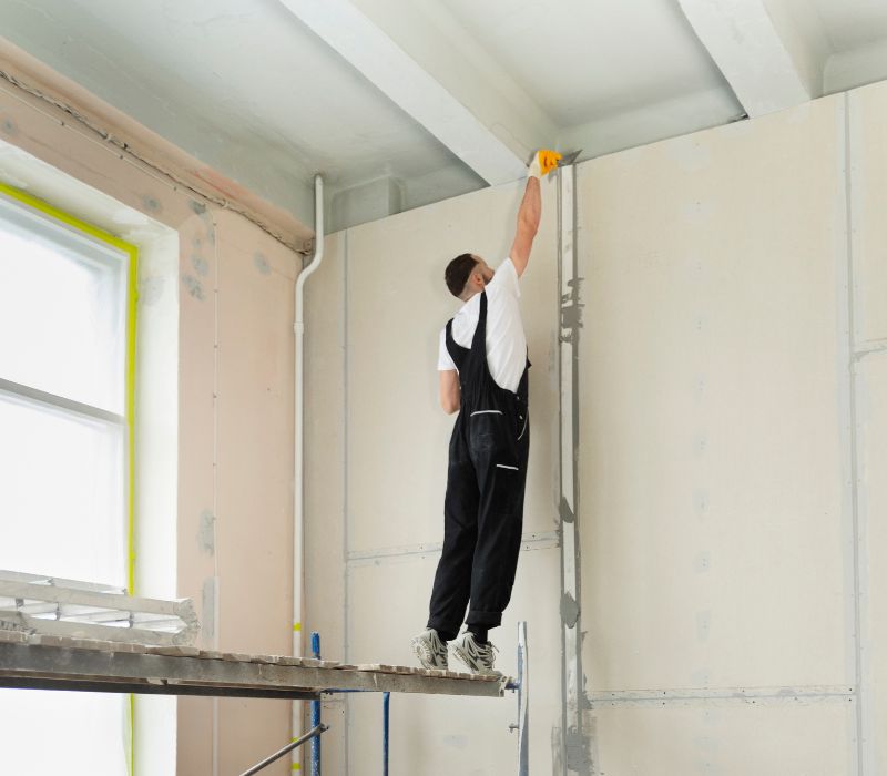 Worker on scaffolding finishing drywall.