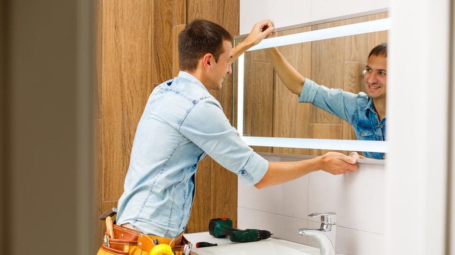 Man installing an illuminated bathroom mirror.