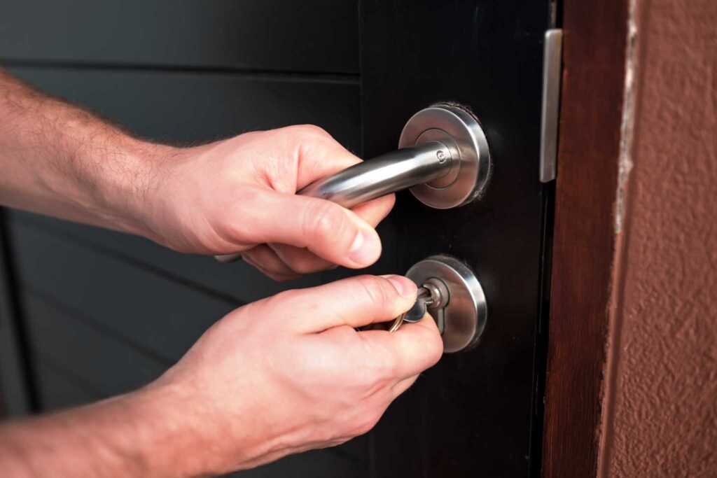 Hands inserting keys into a door lock while gripping the handle.
