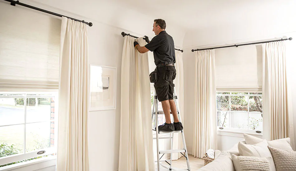 Man on ladder adjusting curtains.