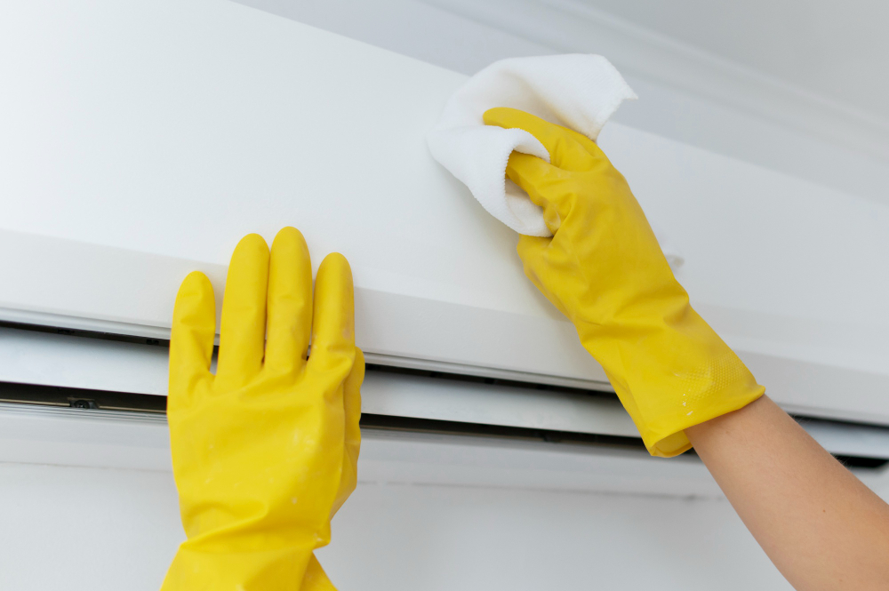 Yellow-gloved hands wiping white AC.