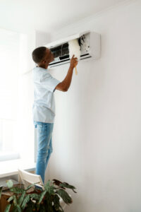 Man cleaning a wall AC unit with a duster.