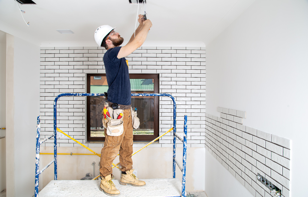 Worker in safety gear installing ceiling wires on a scaffold.