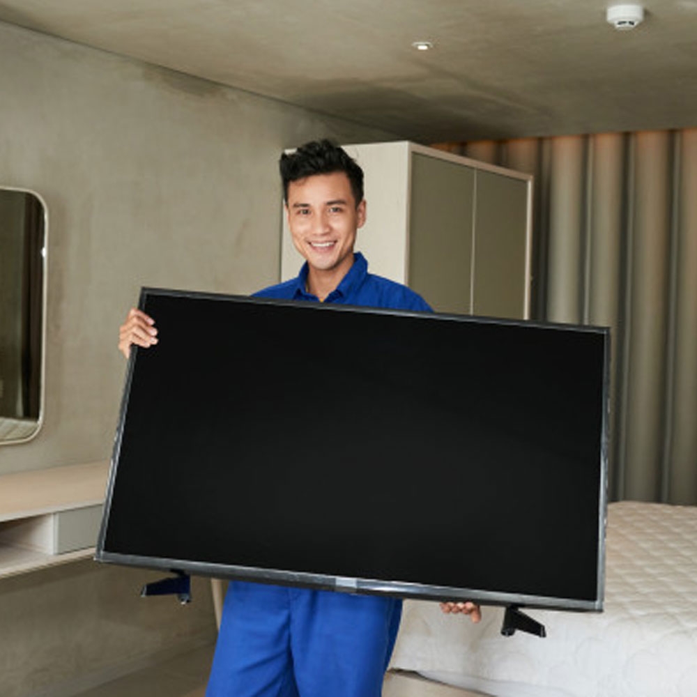 Smiling technician in blue uniform holding a large TV.
