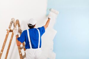Person on ladder painting wall blue.