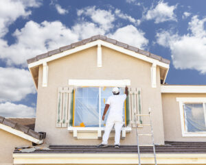Painter on ladder painting house trim.