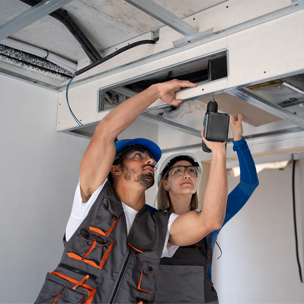 Two workers installing a ceiling with a drill.