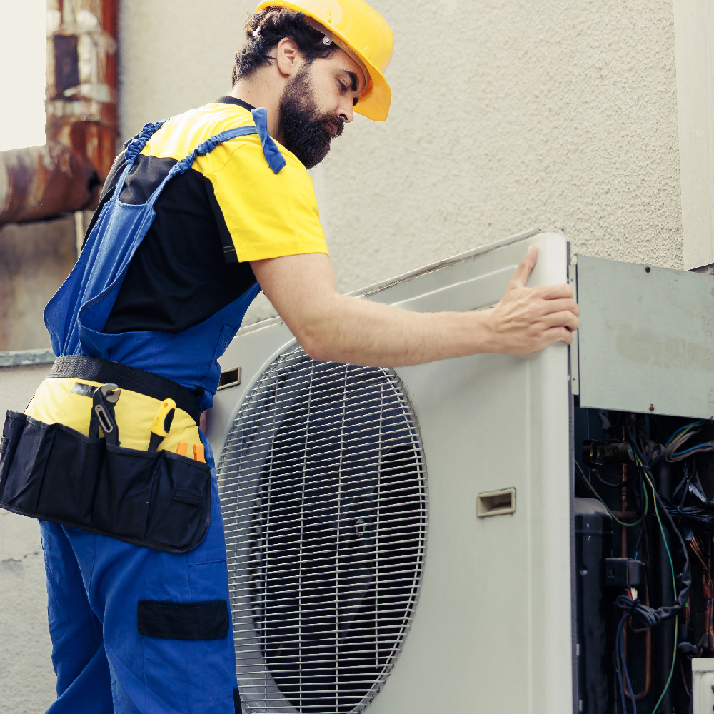 Bearded technician in hard hat and overalls checking HVAC unit