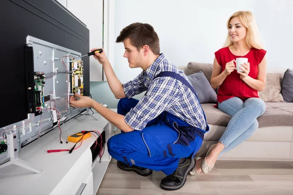 Technician fixes TV, woman watches.
