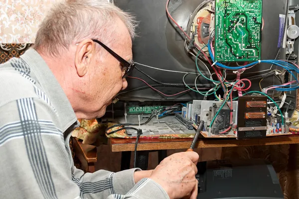 Older man in glasses repairing a TV.