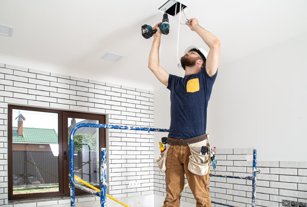 Electrician on scaffolding drilling ceiling for light.