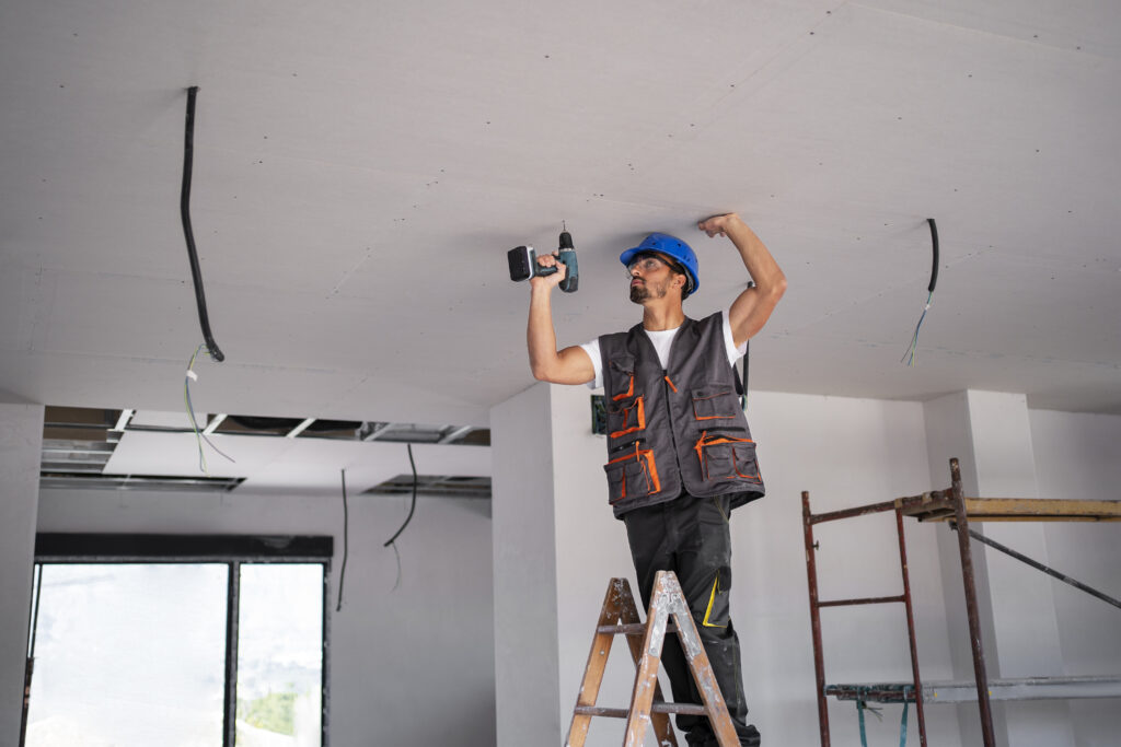 Worker on ladder drilling ceiling.