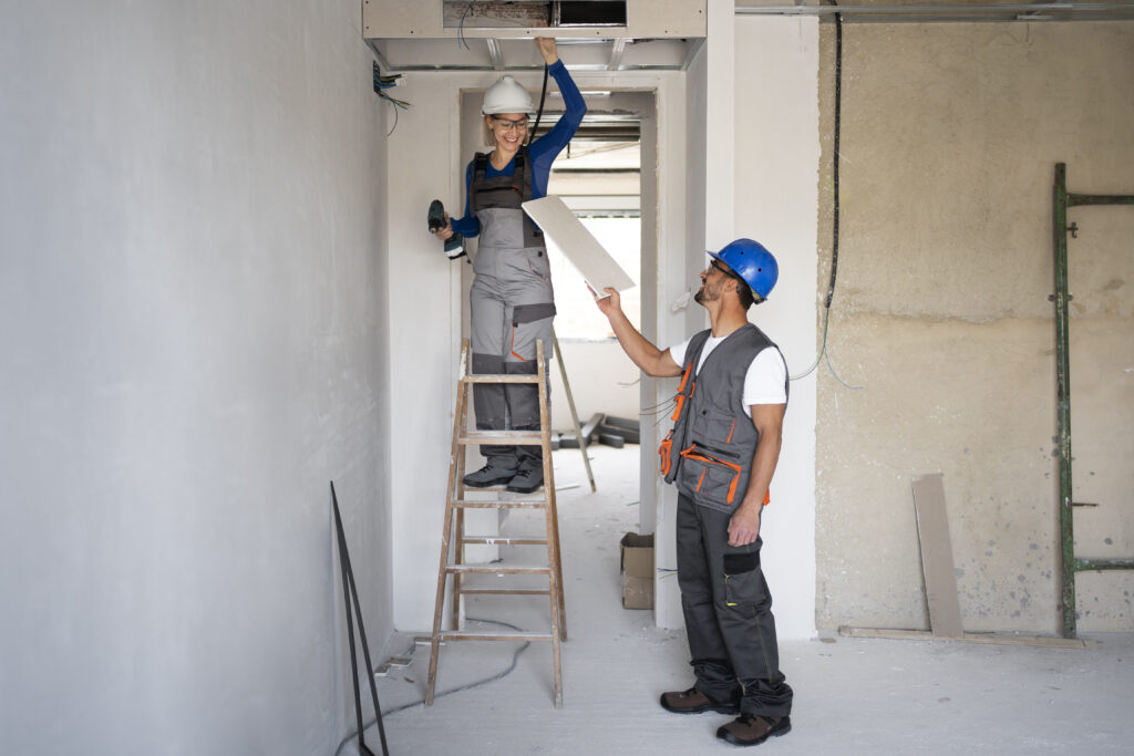 Two workers installing a ceiling panel.