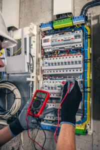 Electrician with multimeter at electrical panel.