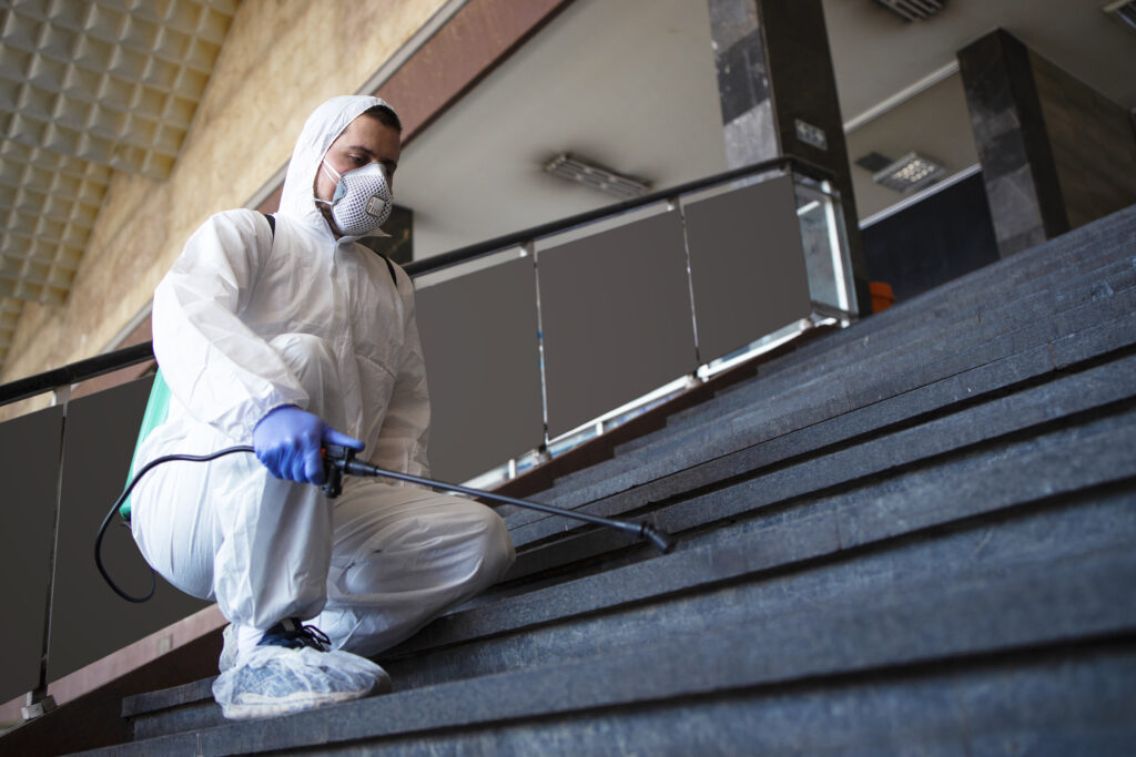Person in white chemical protection suit disinfecting public corridors and steps to stop spreading highly contagious corona virus.