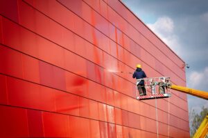 Worker on lift pressure washing building.